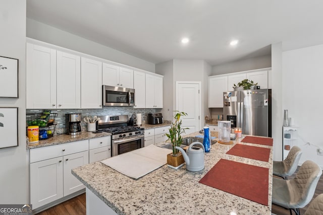 4777 Waxwing St, Hoschton, GA 30548 - kitchen featuring appliances with stainless steel finishes, white cabinets, tasteful backsplash, and an island with sink