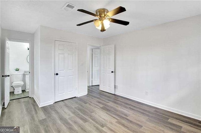 unfurnished bedroom with wood finished floors, baseboards, ensuite bathroom, and ceiling fan