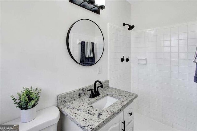 full bathroom featuring a tile shower, vanity, and toilet