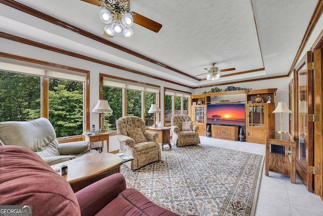 living room with a ceiling fan, a raised ceiling, a textured ceiling, and ornamental molding