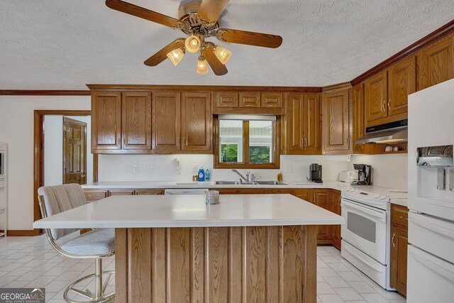 kitchen featuring white appliances, light countertops, a textured ceiling, under cabinet range hood, and a sink