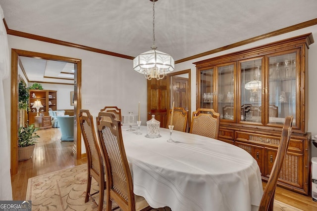 dining area with crown molding, a notable chandelier, and light wood-style flooring