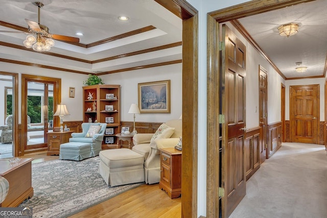 sitting room with wainscoting, a ceiling fan, ornamental molding, and a decorative wall
