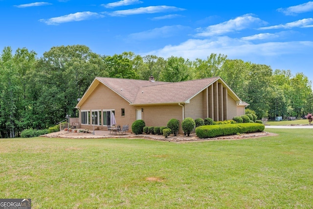 back of house featuring a lawn, a shingled roof, a patio area, and brick siding