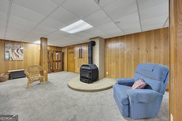 sitting room featuring carpet floors, a wood stove, a paneled ceiling, and wooden walls
