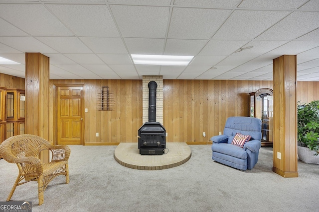living area featuring wood walls, carpet, a wood stove, and a drop ceiling
