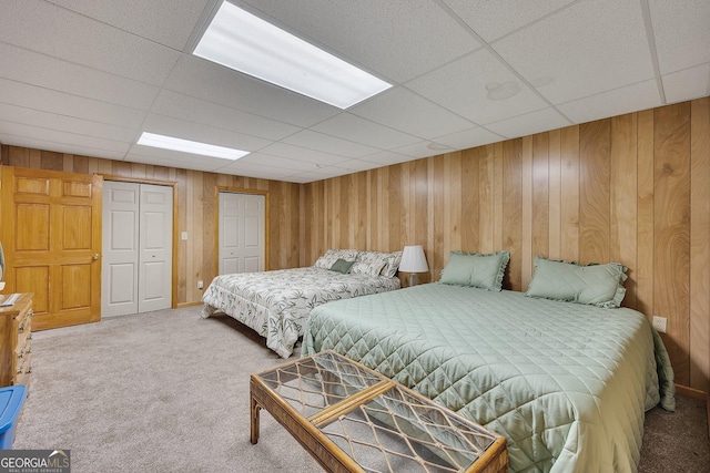 carpeted bedroom featuring wood walls and a drop ceiling