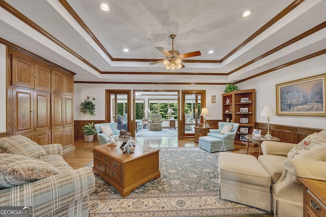 living room with ornamental molding, wainscoting, a ceiling fan, and a tray ceiling