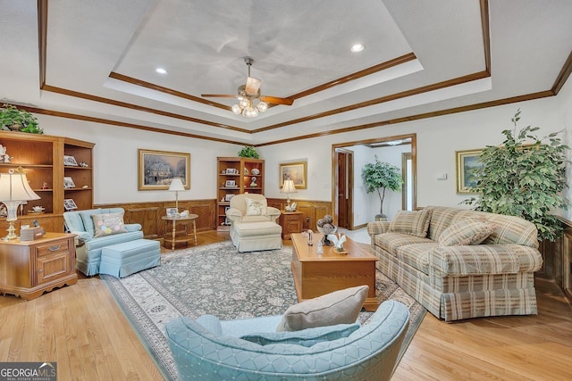 living room with ornamental molding, a raised ceiling, a wainscoted wall, and light wood-style flooring