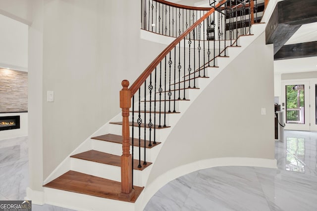 stairway with marble finish floor, a high ceiling, and a fireplace