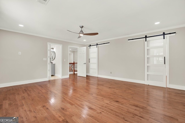 unfurnished living room featuring ornamental molding, a ceiling fan, a barn door, and wood finished floors