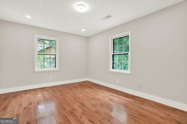unfurnished room with baseboards, visible vents, a wealth of natural light, and hardwood / wood-style floors