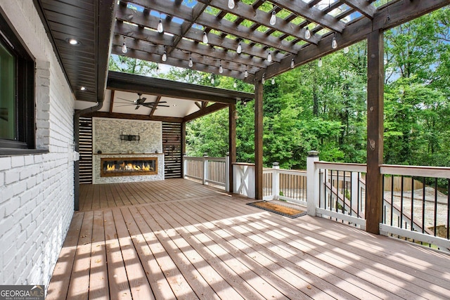 wooden deck featuring a pergola, a glass covered fireplace, and ceiling fan