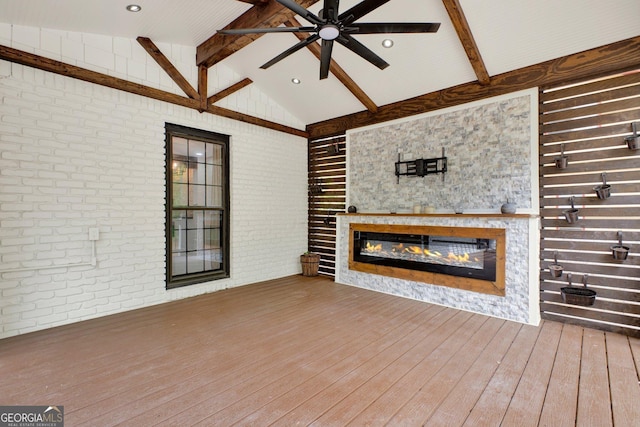 unfurnished living room featuring ceiling fan, brick wall, beam ceiling, wood finished floors, and a glass covered fireplace