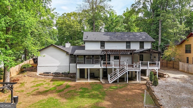 rear view of property featuring a chimney, a deck, stairway, fence, and a shingled roof