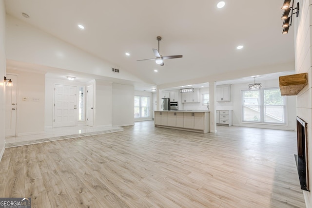 9985 Lake Forest Way, Roswell, GA 30076 - unfurnished living room with visible vents, a fireplace, vaulted ceiling, ceiling fan with notable chandelier, and light wood finished floors