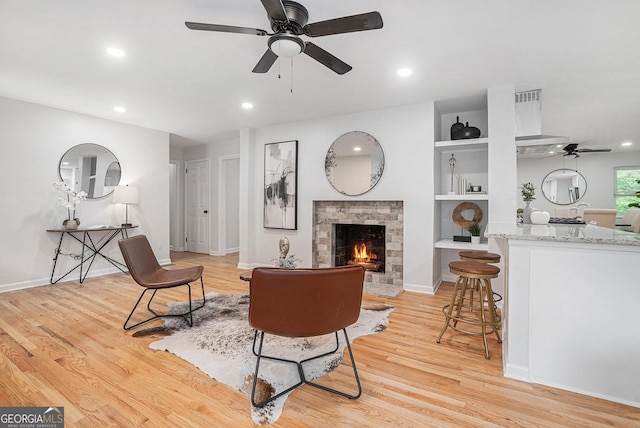 living room with a ceiling fan, recessed lighting, light wood-style flooring, a lit fireplace, and built in features