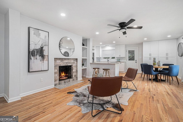 living area featuring light wood-style flooring, a fireplace with flush hearth, a ceiling fan, baseboards, and recessed lighting