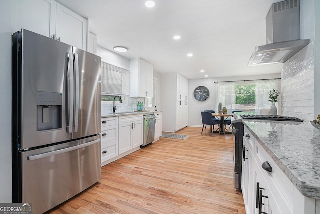 kitchen with appliances with stainless steel finishes, wall chimney range hood, a sink, recessed lighting, and white cabinetry