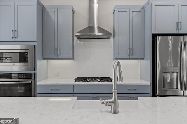 kitchen featuring backsplash, appliances with stainless steel finishes, gray cabinetry, a sink, and wall chimney exhaust hood