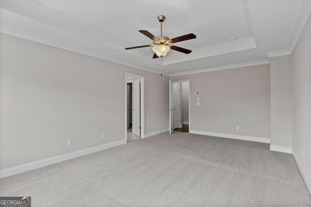 empty room with ornamental molding, light carpet, baseboards, a tray ceiling, and a ceiling fan