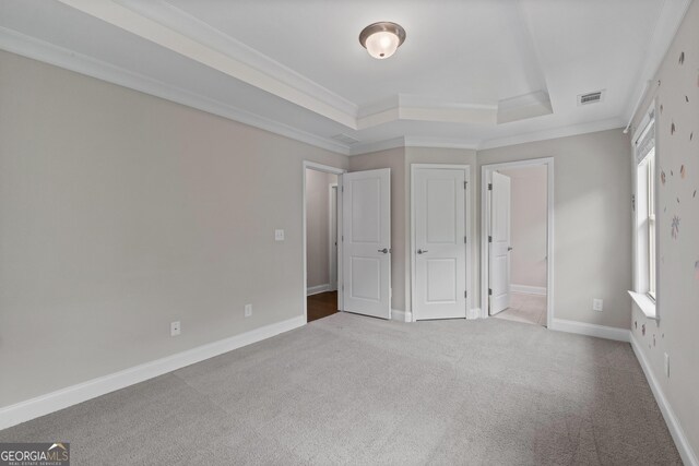 unfurnished bedroom featuring visible vents, carpet floors, baseboards, ornamental molding, and a tray ceiling