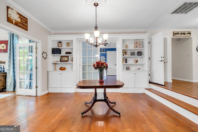 dining space with light wood-style floors, visible vents, built in shelves, an inviting chandelier, and ornamental molding