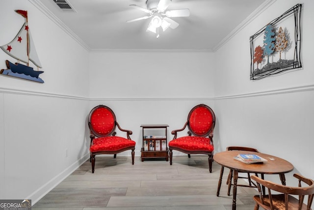 sitting room featuring a ceiling fan, baseboards, wood finished floors, visible vents, and ornamental molding