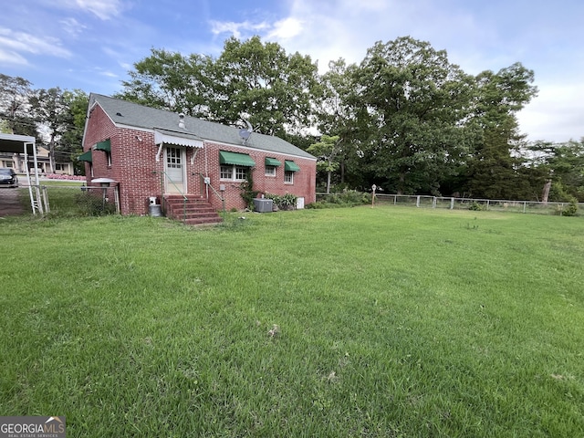 rear view of property with fence, brick siding, entry steps, central AC unit, and a lawn