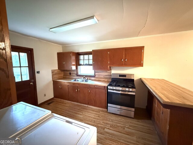 kitchen with crown molding, gas stove, light countertops, a sink, and dark wood-style floors