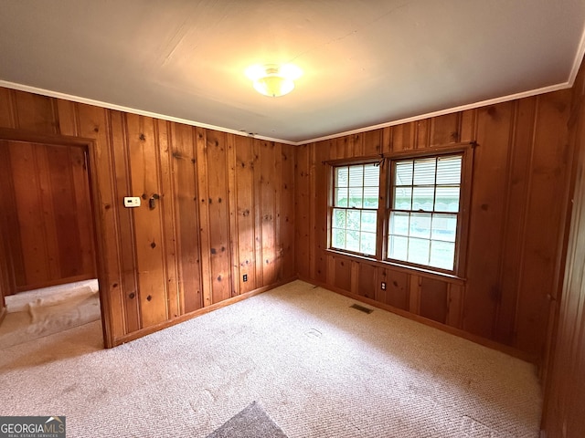 carpeted empty room featuring wood walls, visible vents, ornamental molding, and baseboards