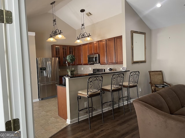 kitchen with dark countertops, a breakfast bar, stainless steel appliances, a peninsula, and decorative backsplash
