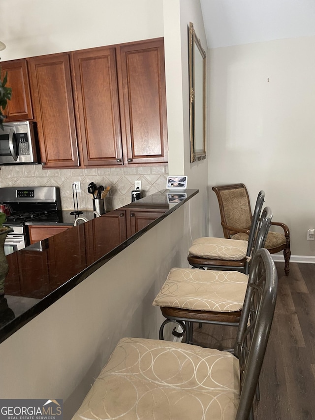 kitchen featuring appliances with stainless steel finishes, brown cabinetry, baseboards, decorative backsplash, and dark wood-type flooring