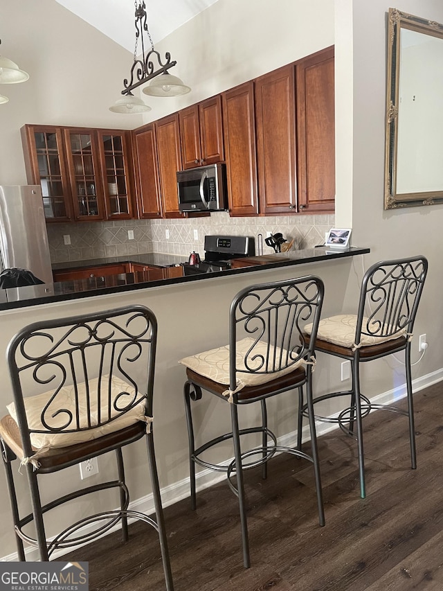 kitchen with stainless steel appliances, dark countertops, a kitchen breakfast bar, and dark wood-type flooring