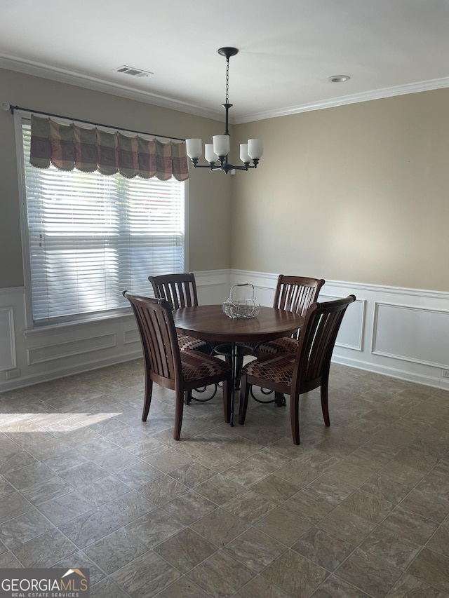 dining area featuring visible vents, crown molding, wainscoting, a chandelier, and a decorative wall