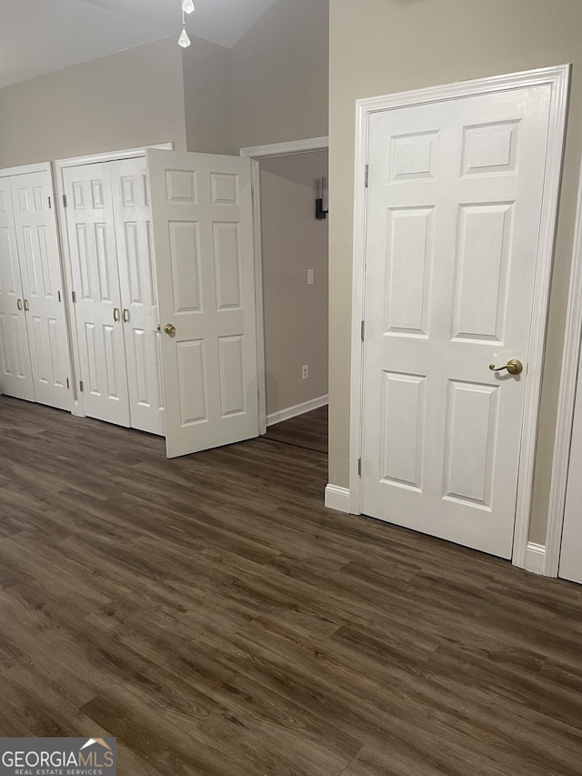 unfurnished bedroom with baseboards, multiple closets, and dark wood-type flooring
