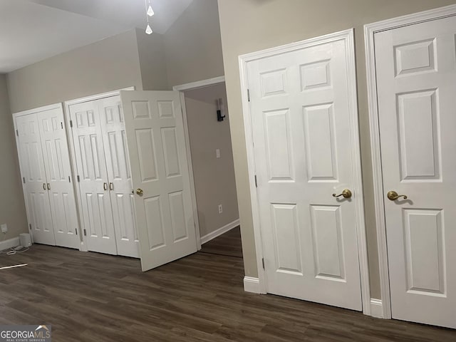 unfurnished bedroom with two closets, baseboards, and dark wood-style floors