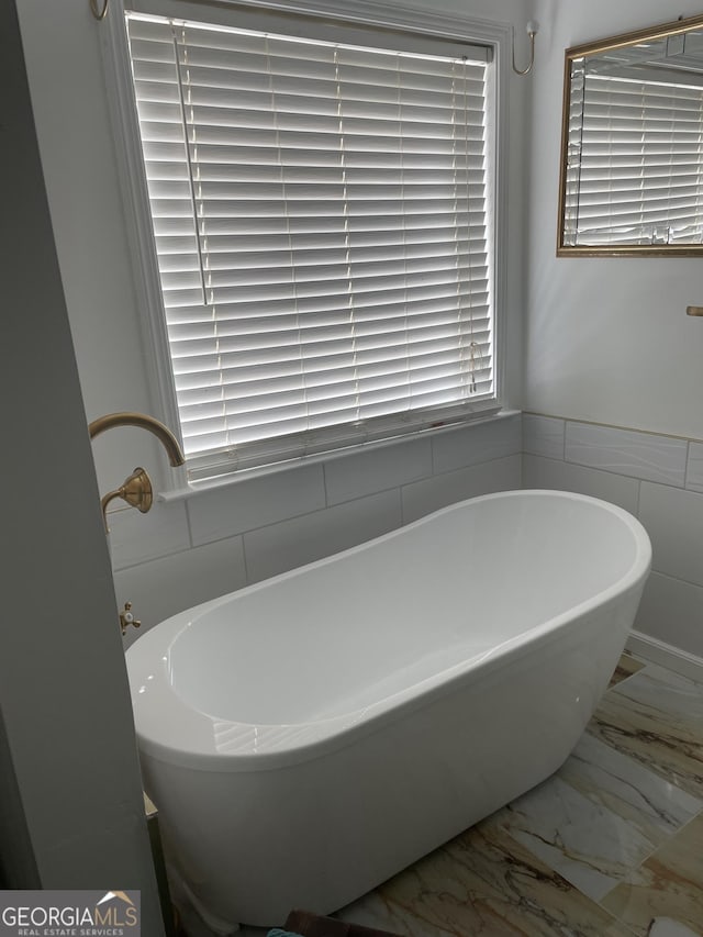 bathroom with marble finish floor and a freestanding bath