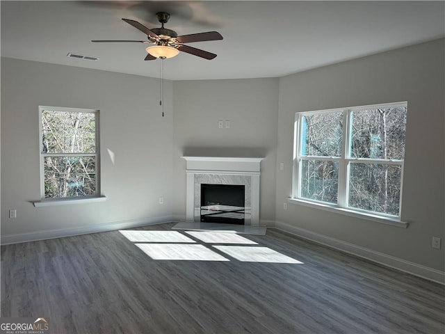 unfurnished living room with plenty of natural light, a ceiling fan, visible vents, a fireplace, and wood finished floors