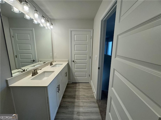 full bathroom with double vanity, a sink, baseboards, and wood finished floors