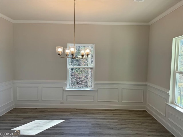 unfurnished dining area with crown molding, a chandelier, dark wood finished floors, and a wainscoted wall