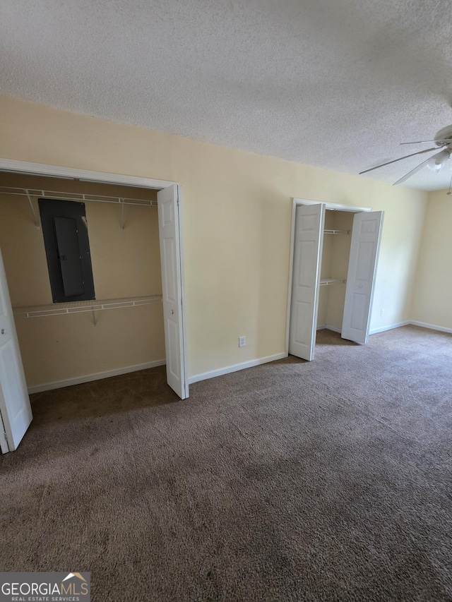unfurnished bedroom with electric panel, a textured ceiling, baseboards, two closets, and carpet