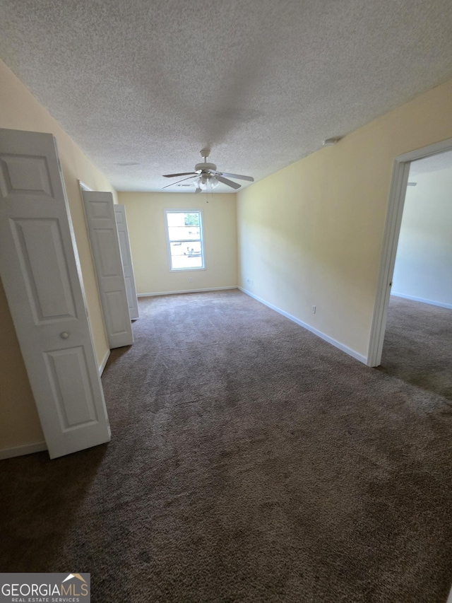 empty room with baseboards, a ceiling fan, a textured ceiling, and dark carpet