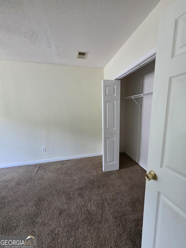 unfurnished bedroom with visible vents, a closet, dark carpet, baseboards, and a textured ceiling