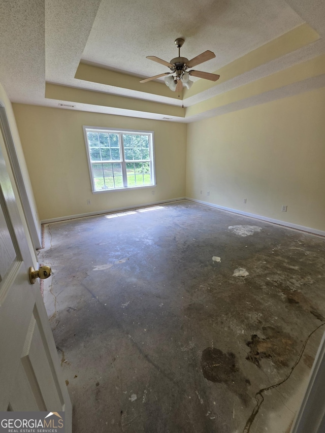 unfurnished room with a textured ceiling, a tray ceiling, concrete floors, and ceiling fan