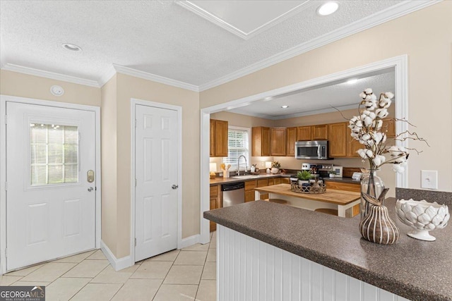 kitchen featuring brown cabinetry, dark countertops, a sink, light tile patterned floors, and stainless steel appliances