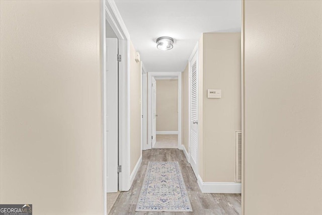 corridor with baseboards, visible vents, and light wood finished floors