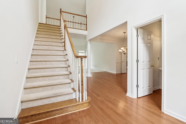stairs with baseboards, an inviting chandelier, a towering ceiling, and wood finished floors