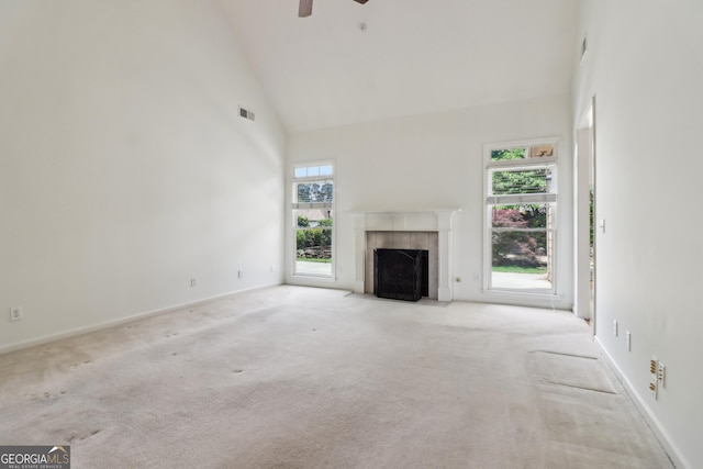 unfurnished living room featuring ceiling fan, high vaulted ceiling, a tiled fireplace, carpet, and visible vents
