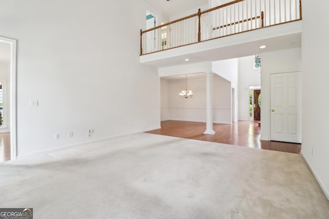 unfurnished living room featuring carpet floors, decorative columns, a towering ceiling, baseboards, and a chandelier